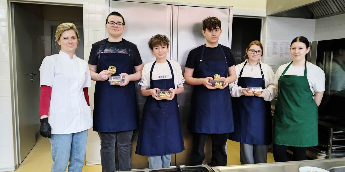 Uczniowie z ciastem stoją w kuchni